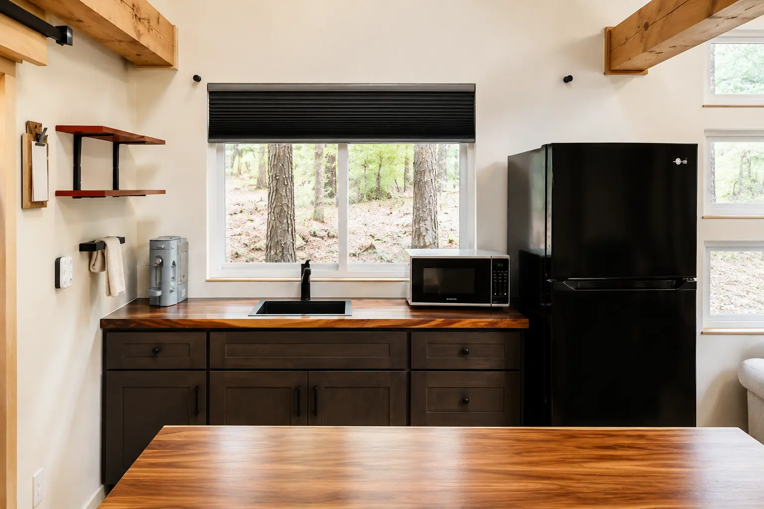 Kitchen sink, microwave and full-size refrigerator with woods outside