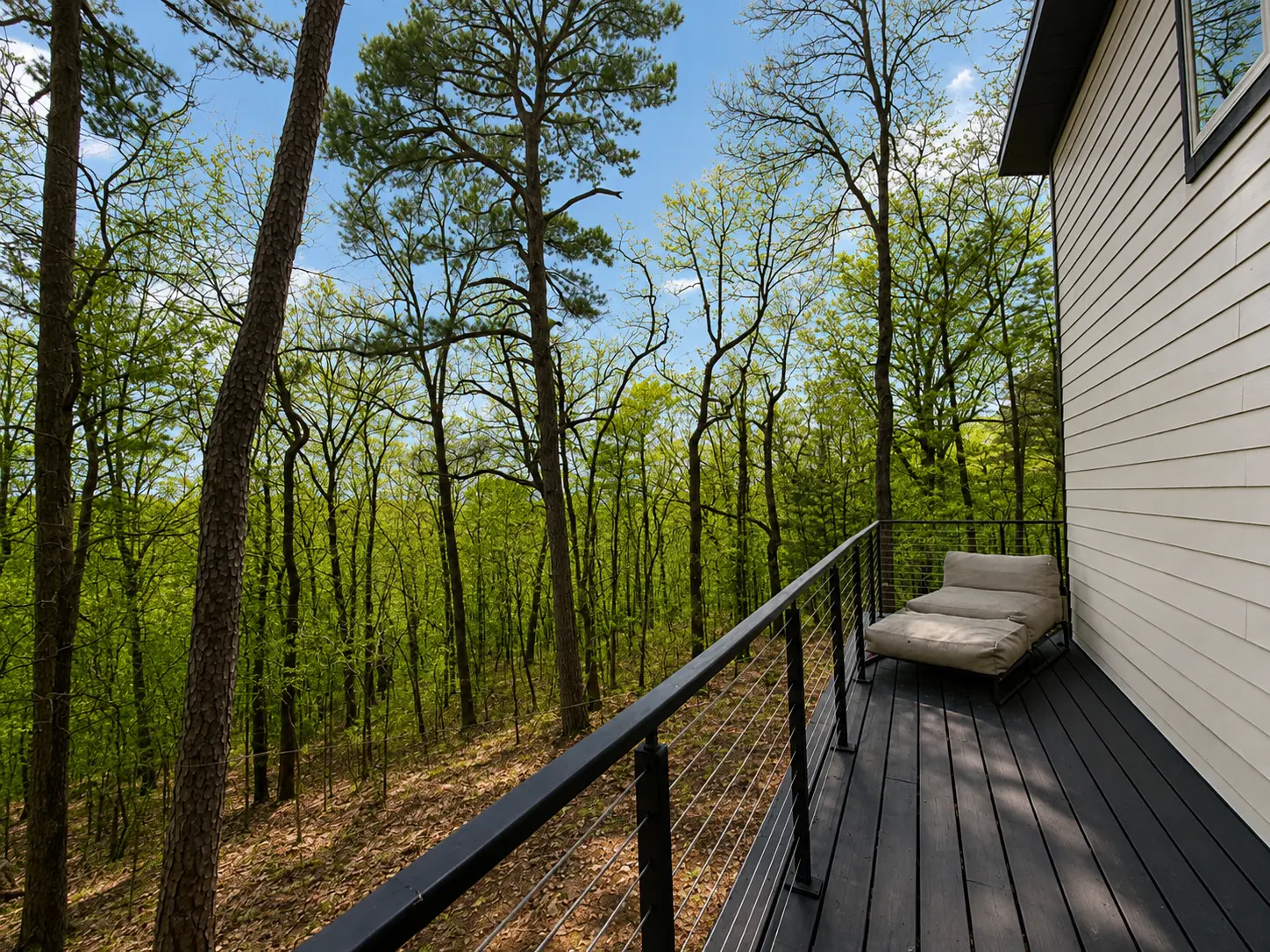 Private black deck with cable railing overlooking the green forest